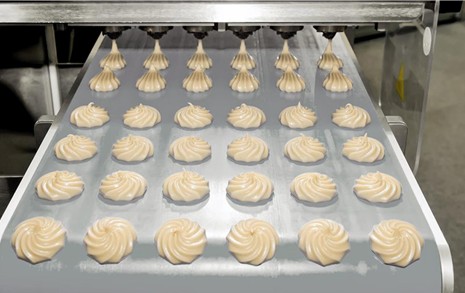 Uncooked bakery goods being piped onto a steel conveyor belt prior to going into a continuous oven